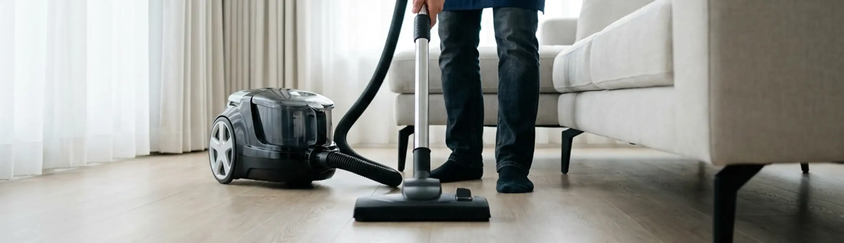 Professional house cleaner vacuuming a living room floor with a canister vacuum cleaner, Hollywood, FL.