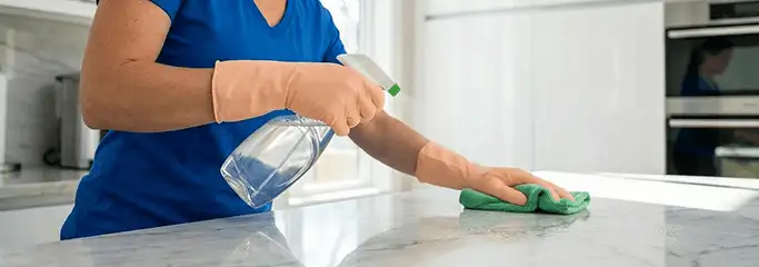 Maid service worker spraying and wiping a kitchen countertop with a microfiber cloth for sanitizing, Hollywood, FL.