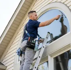 Professional window cleaner on a ladder using a squeegee to clean an exterior arched window, Hollywood, FL.
