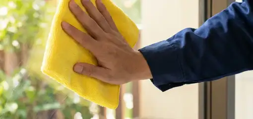 House cleaner wiping a glass window with a yellow microfiber cloth for streak-free cleaning, Hollywood, FL.